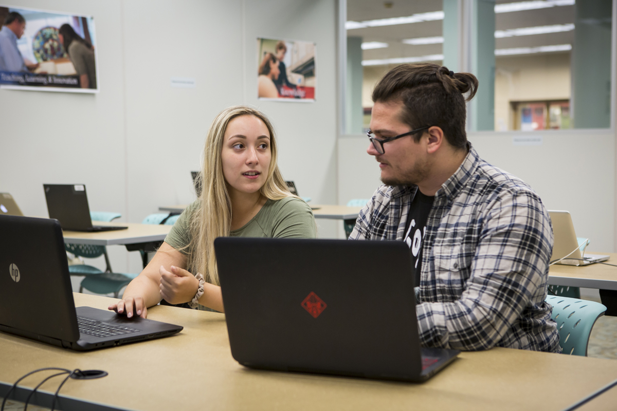 A woman and man seated at a table with laptops in front of them