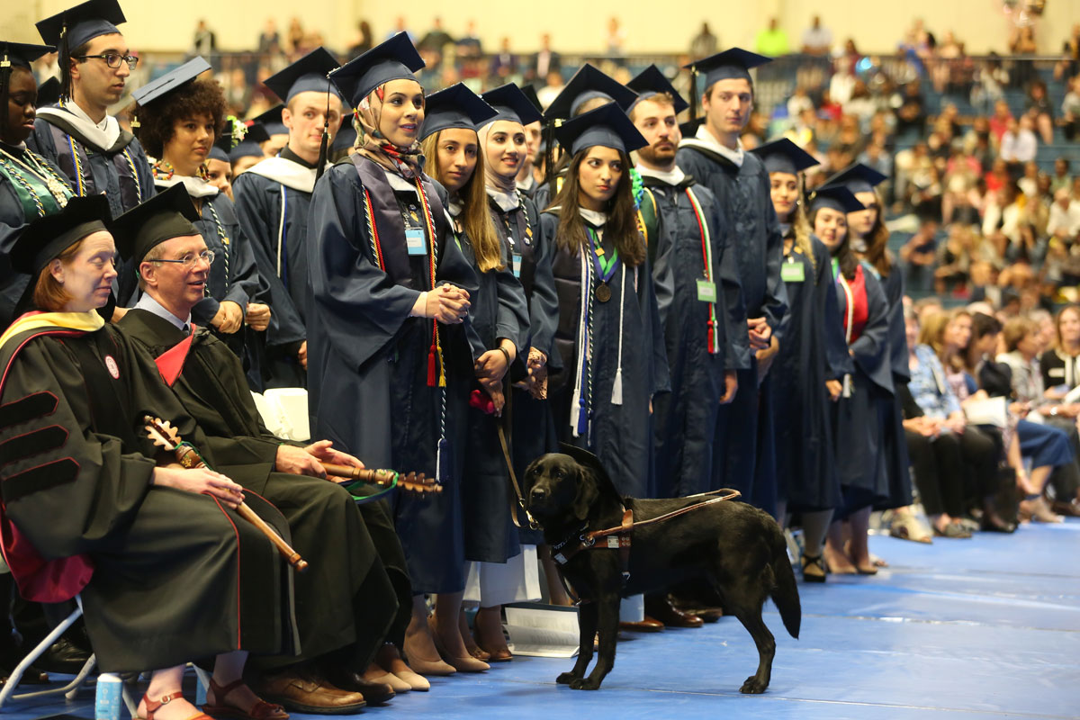 Line of Drew graduates in a row including a woman with a guide dog